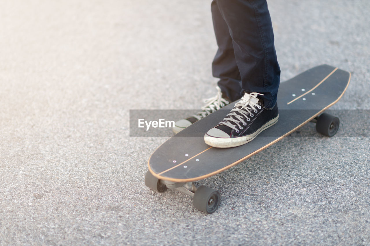 Low section of person with skateboard standing on road