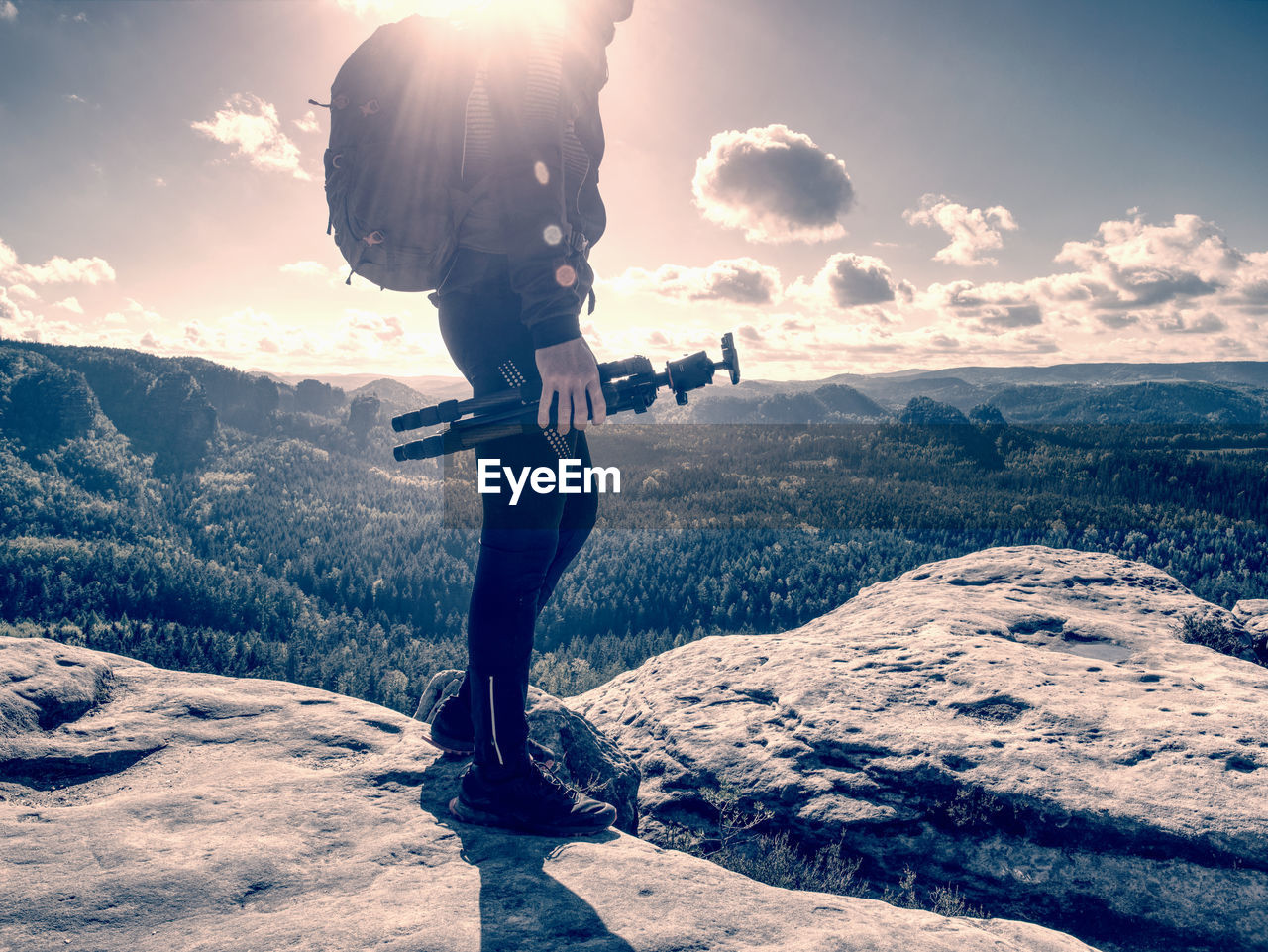 Man creator and photographer is setting up tripod for standing on rocky cliff. nature photograper