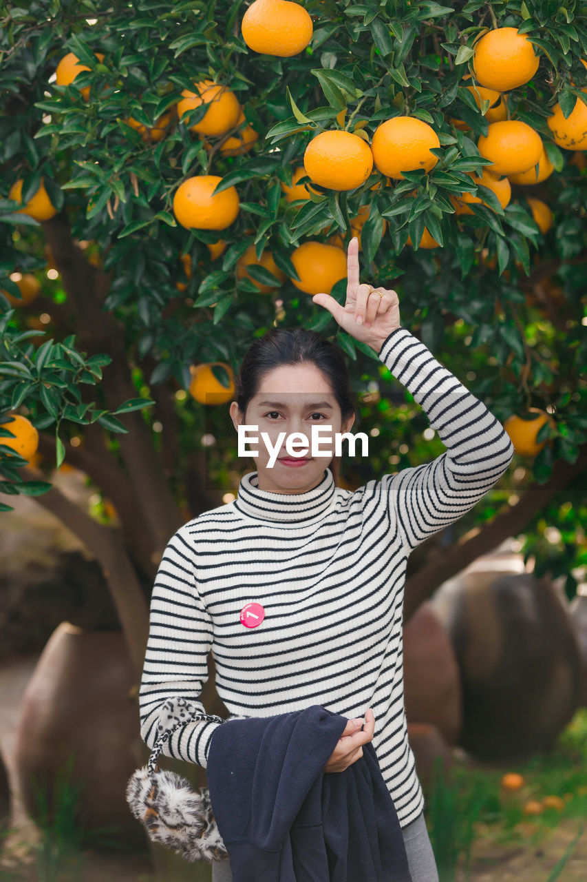 Portrait of woman standing pointing at oranges growing on tree