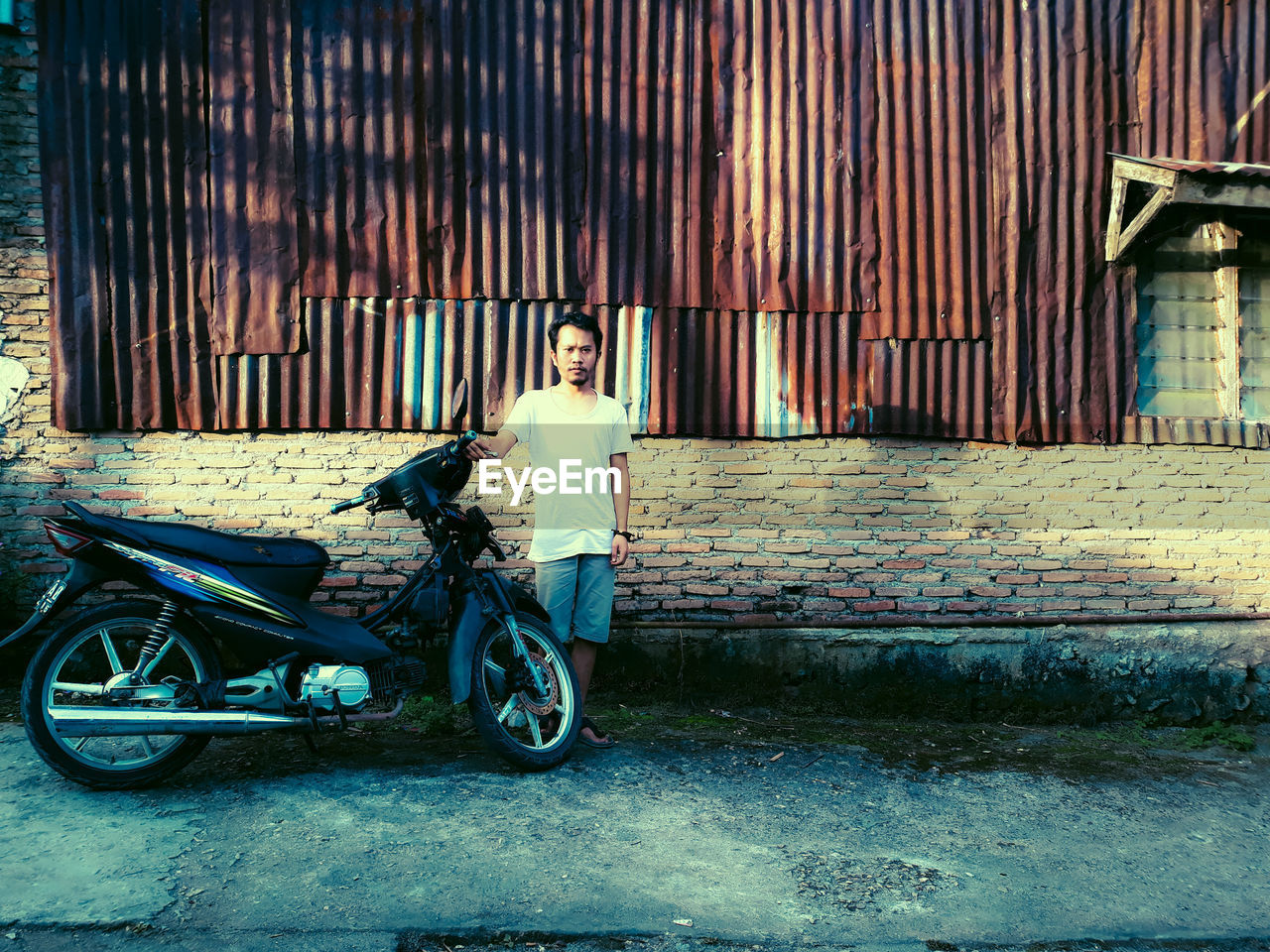 PORTRAIT OF BOY WITH BICYCLE STANDING AGAINST WALL