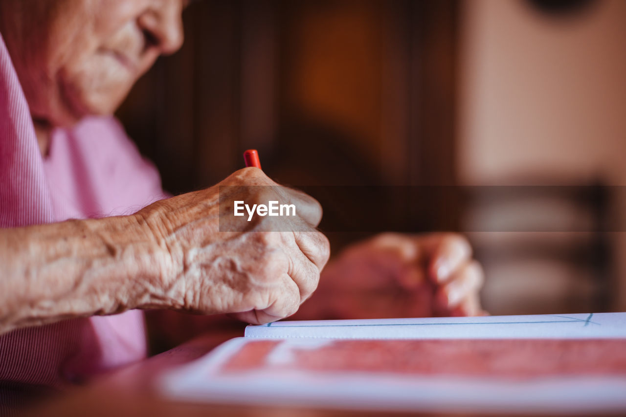 Side view of a senior woman with alzheimer's mental health issues painting on a notebook inside her home