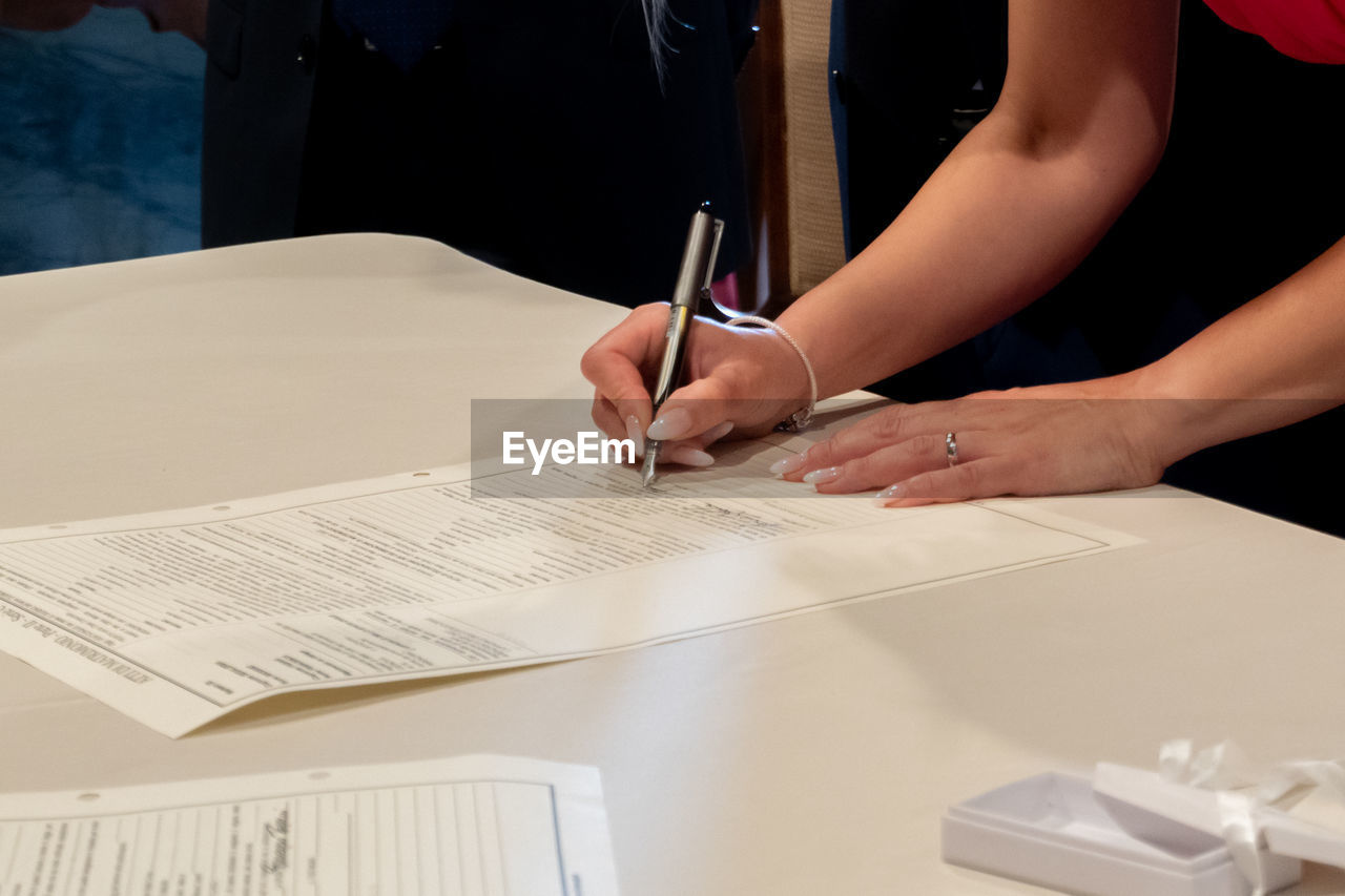 hand, adult, table, business, indoors, paper, occupation, writing, pen, one person, office supplies, document, women, working, business finance and industry, desk, creativity, midsection, office, furniture, holding