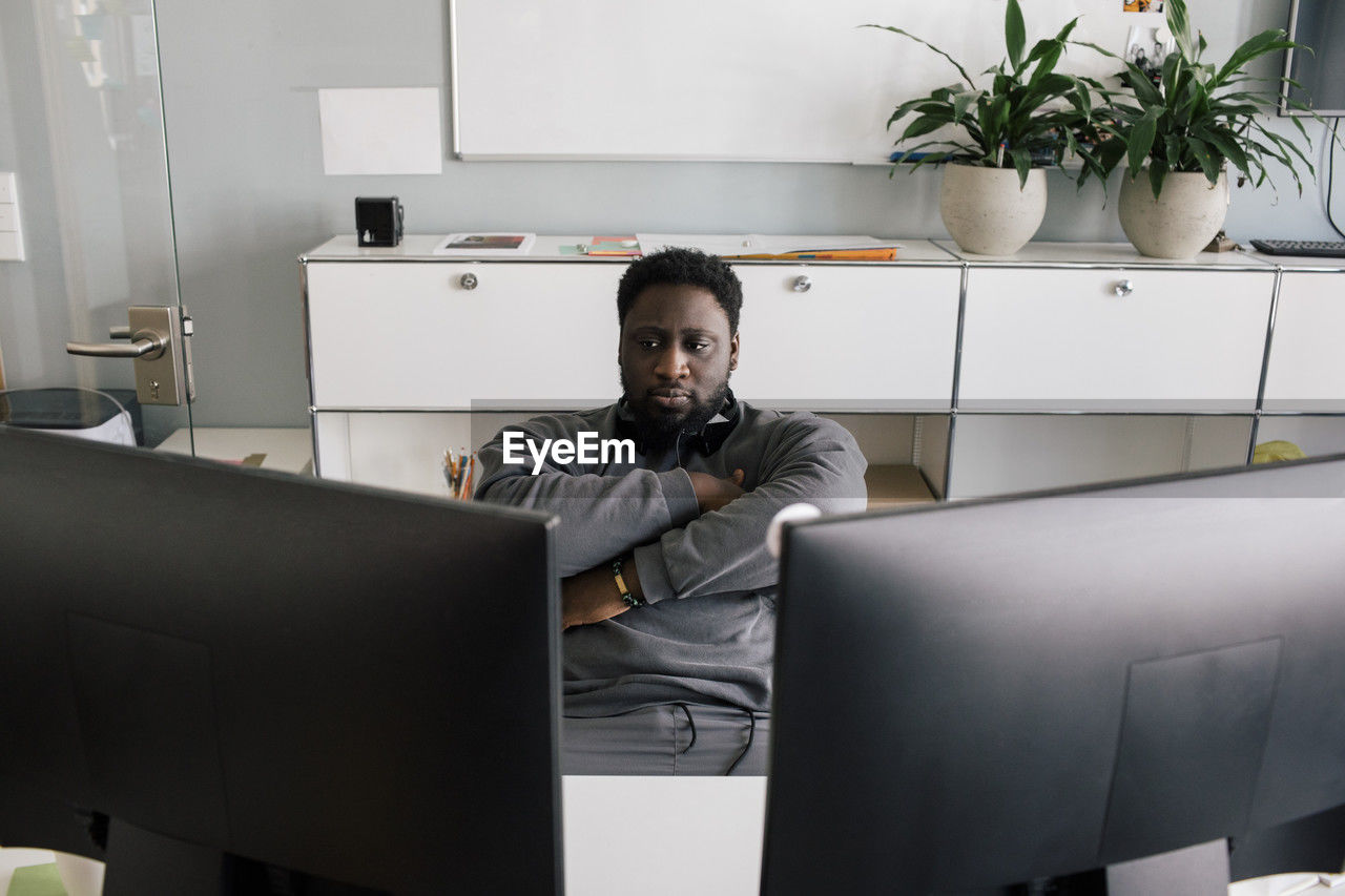 Businessman with arms crossed looking at computers while sitting at office