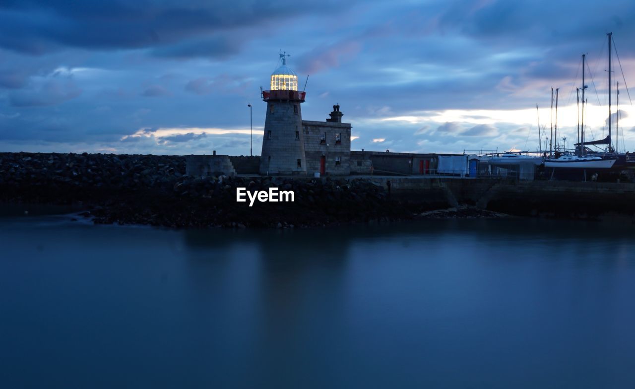 Lighthouse by sea against sky at dusk