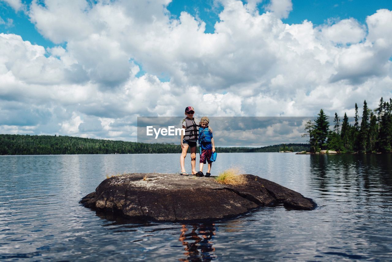 Low angle view of boys standing on rock in lake