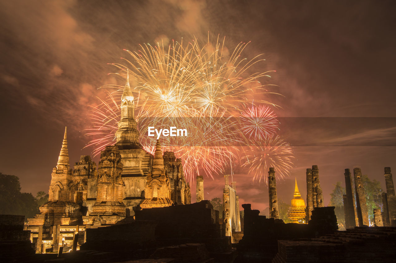 FIREWORK DISPLAY IN ILLUMINATED BUILDING AGAINST SKY AT NIGHT