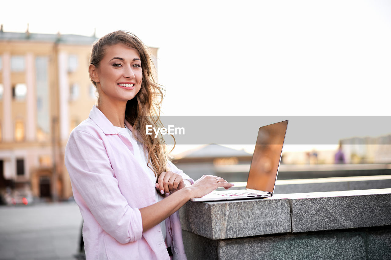 Portrait of smiling woman using laptop on retaining wall