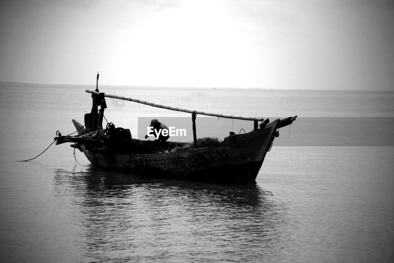 Man crouching in fishing boat on sea against sky