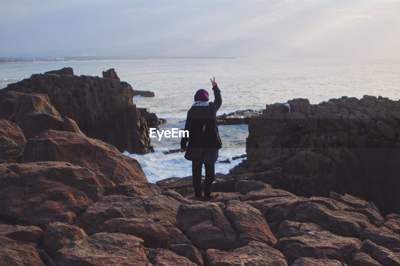 Rear view of woman standing on rock at shore