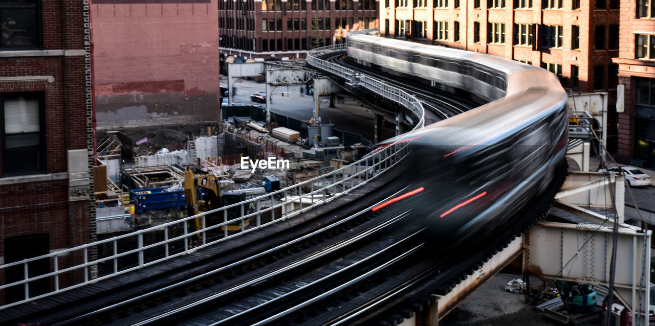 Blurred motion of train on railway bridge amidst buildings in city