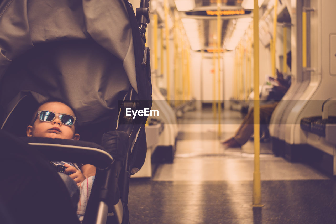 Cute boy relaxing on baby carriage in train