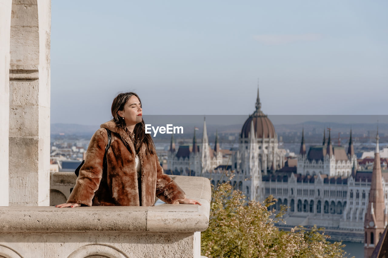 Portrait of girl standing on balcony overlooking city of budapest, hungary