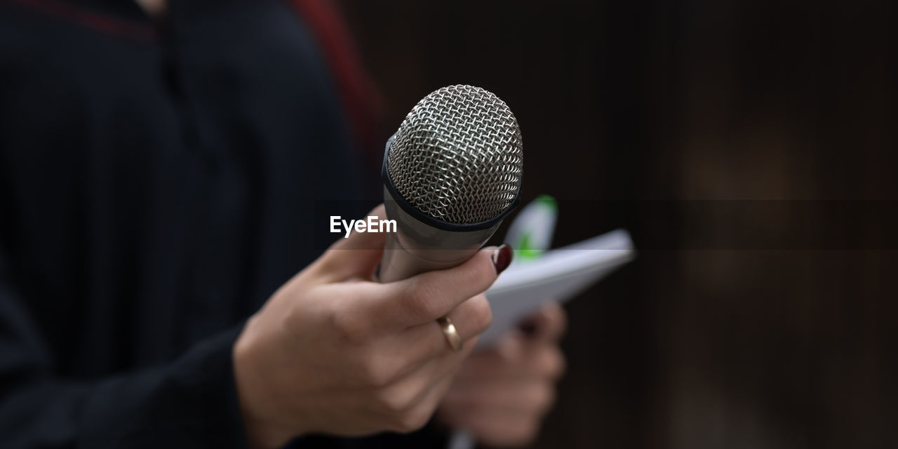 Female journalist in action at news conference, holding microphones and writing notes