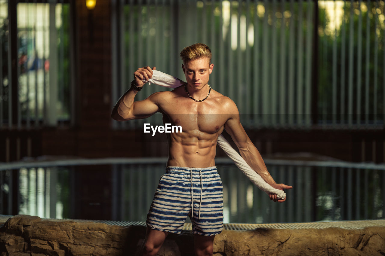 Portrait of shirtless muscular man standing by swimming pool