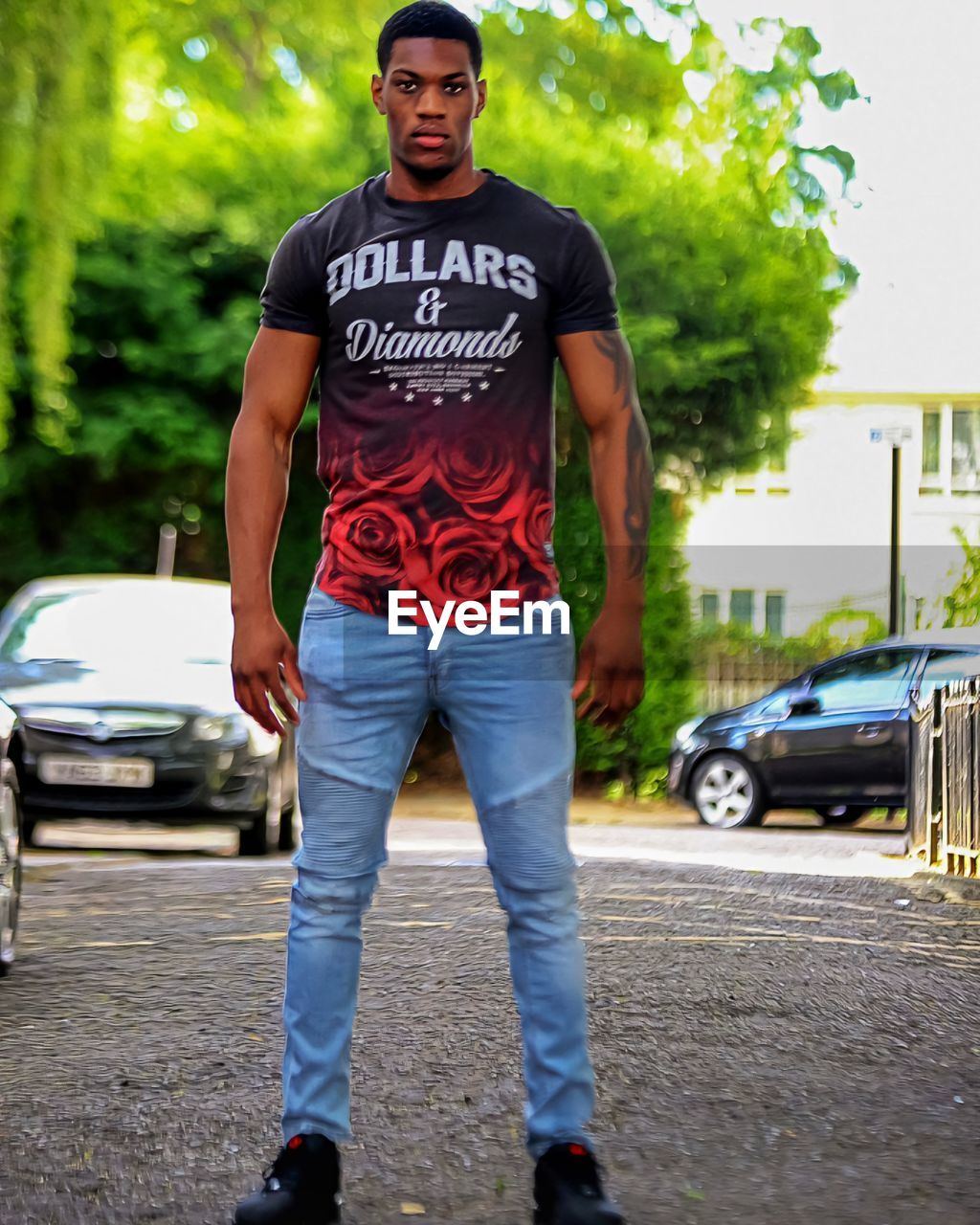 one person, car, motor vehicle, transportation, city, portrait, standing, adult, full length, mode of transportation, men, casual clothing, looking at camera, front view, young adult, vehicle, street, land vehicle, architecture, clothing, jeans, day, footwear, cool attitude, fashion, person, outdoors, endurance sports