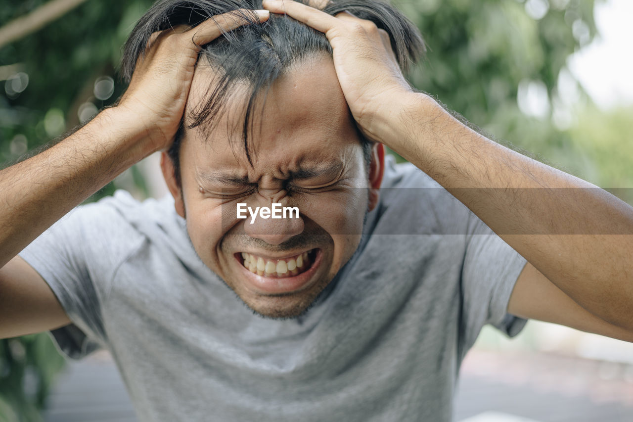 Frustrated man with eyes closed and hand in hair against trees