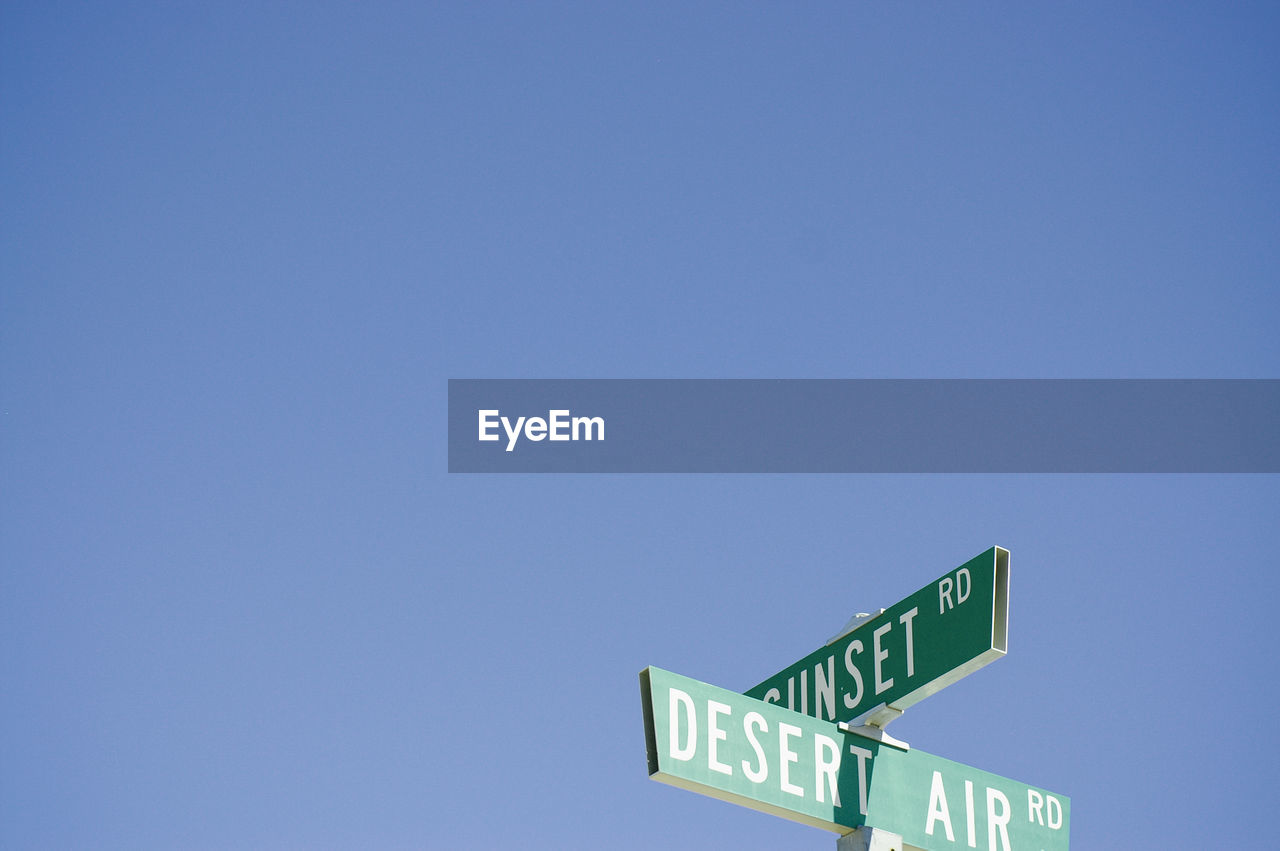 Low angle view of road sign against clear blue sky