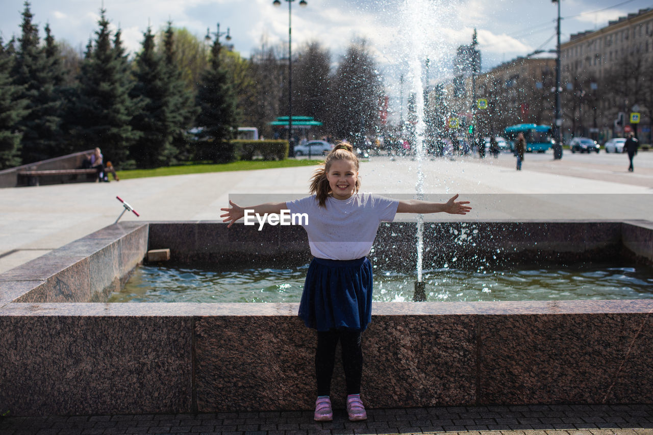 Happy little cute girl having fun in splashes a fountain