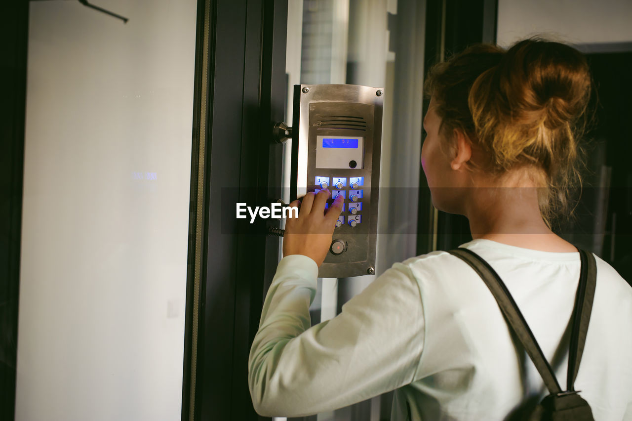 Side view of young woman using intercom