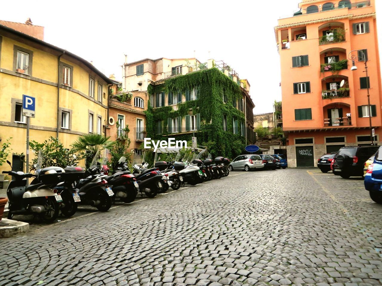 Cobblestone street amidst parked vehicles against buildings