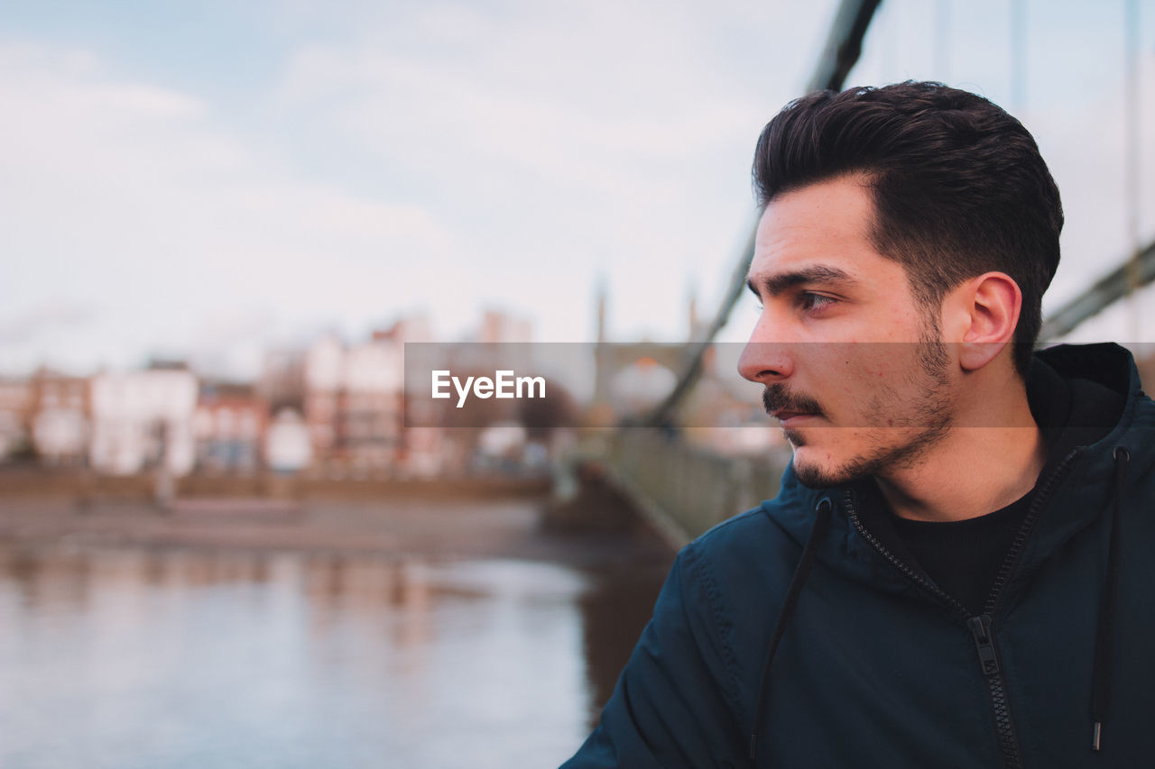 Close-up of thoughtful young man standing by river in city