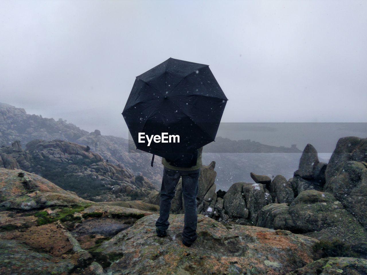 Man with umbrella on a mountain peak with his back to the camera 