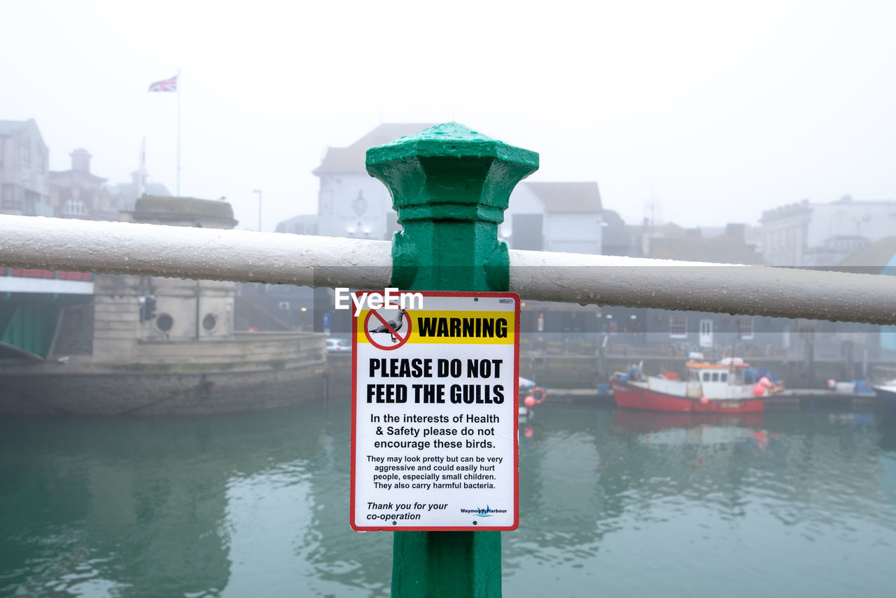 CLOSE-UP OF SIGN BY RIVER IN CITY