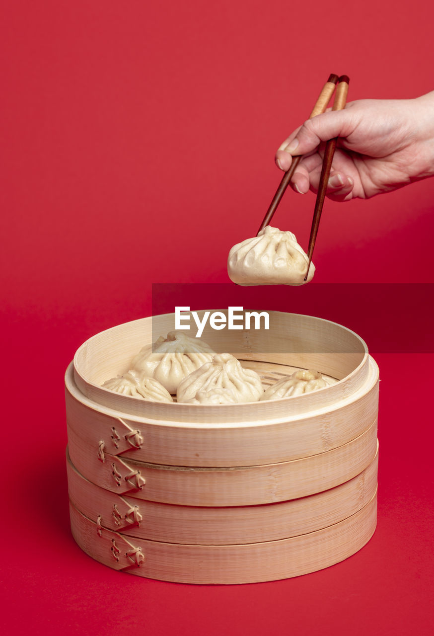 Woman taking a dumpling from the bamboo steamer with the chopsticks, isolated on red background.