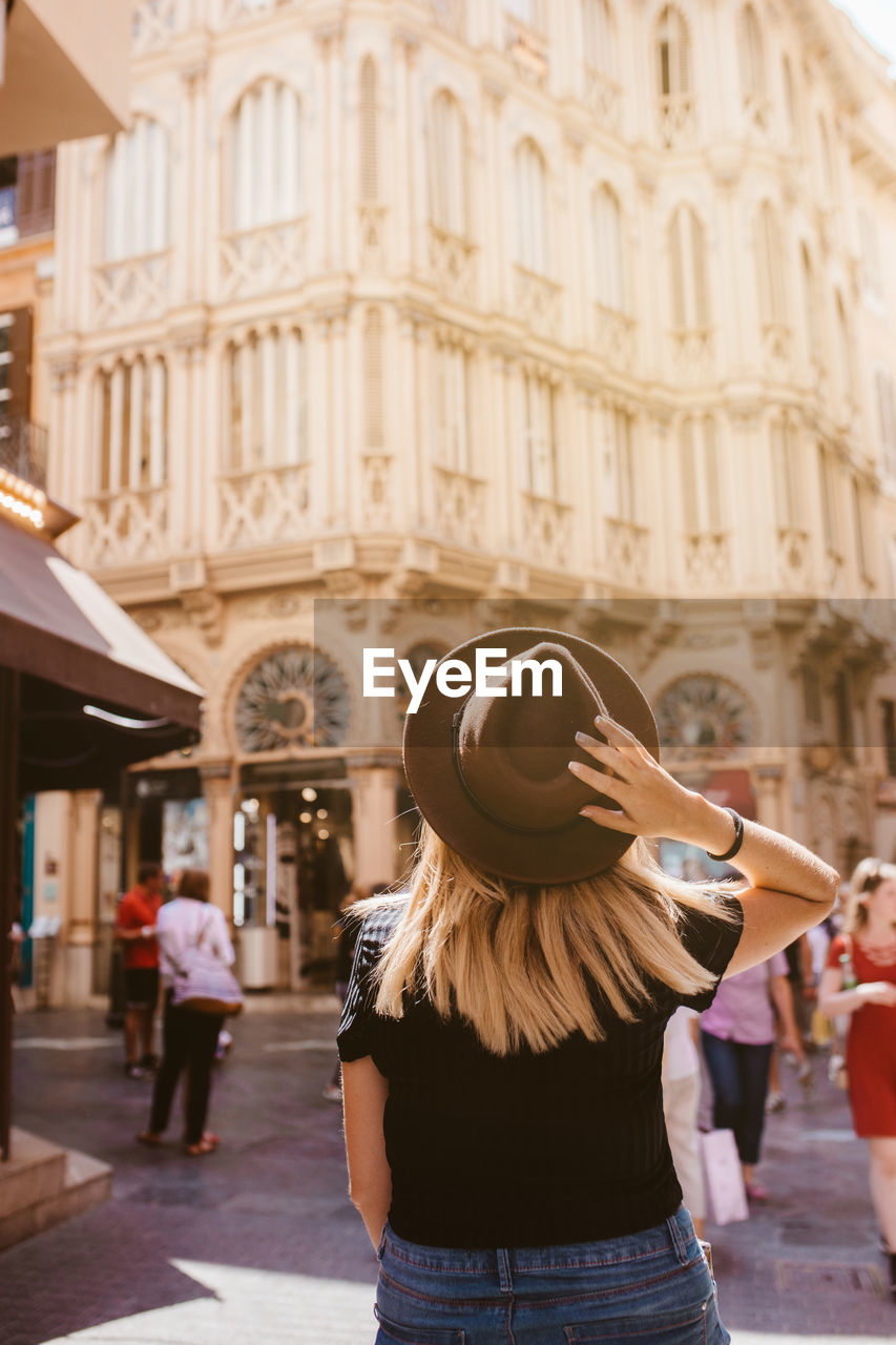 Back view of adventurous traveler touching her hat visiting majorca