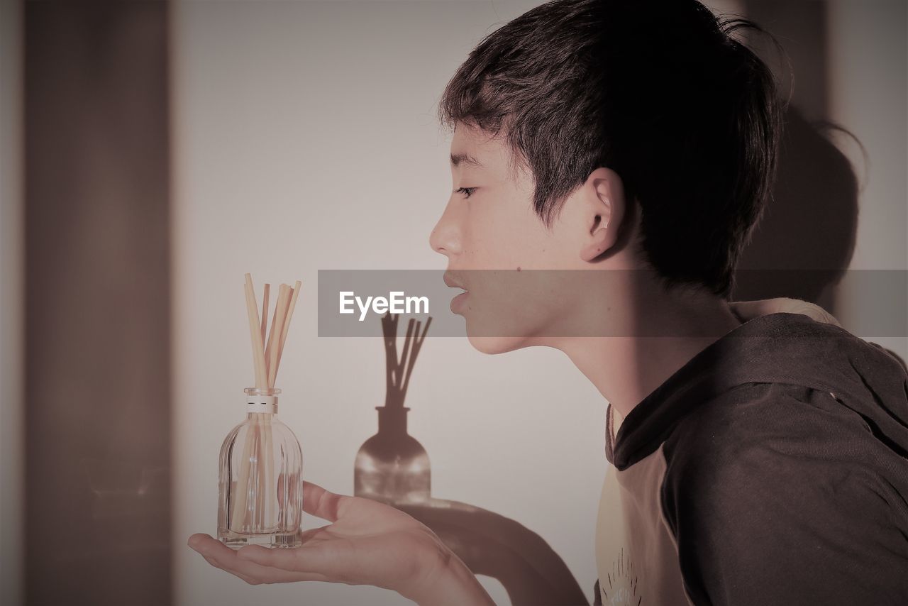 Side view of boy holding container with sticks against wall at home