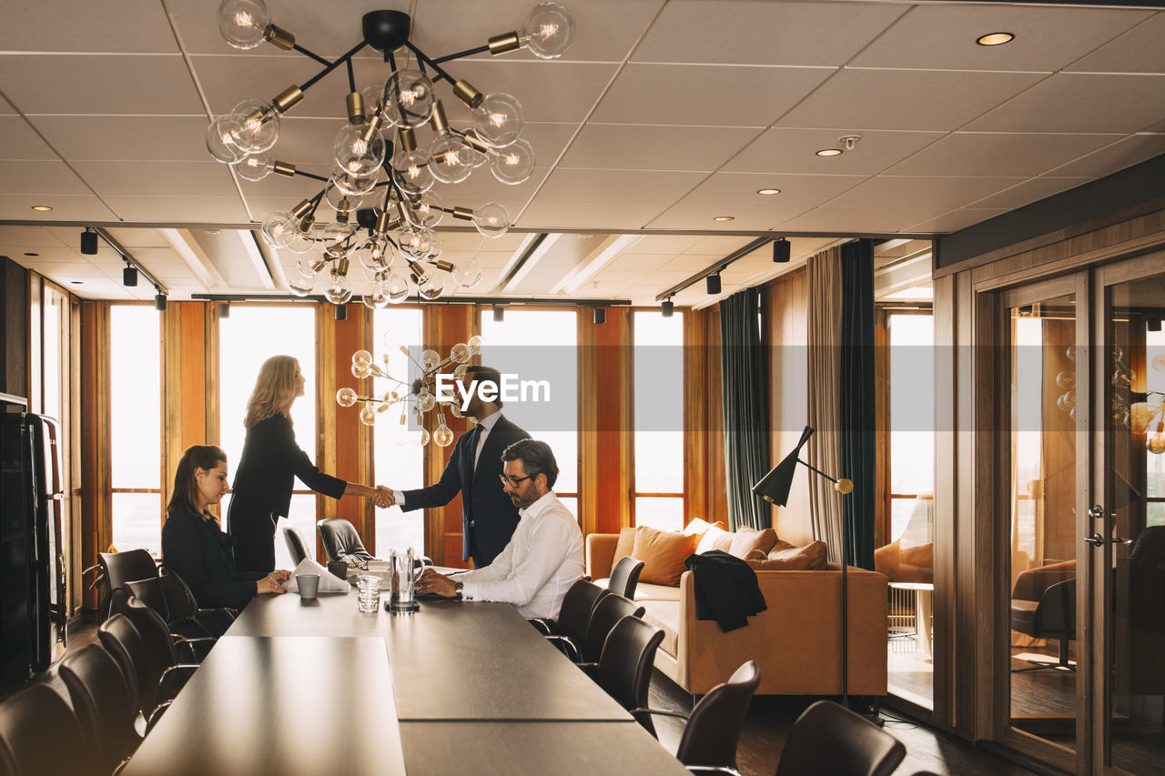 Colleagues shaking hands while lawyers working at table in board room