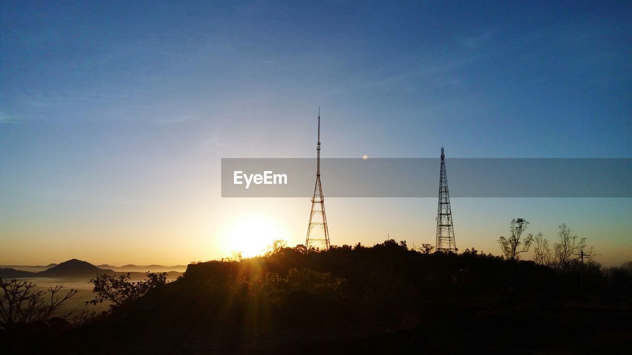 Repeater towers on silhouette mountain against sky during sunset