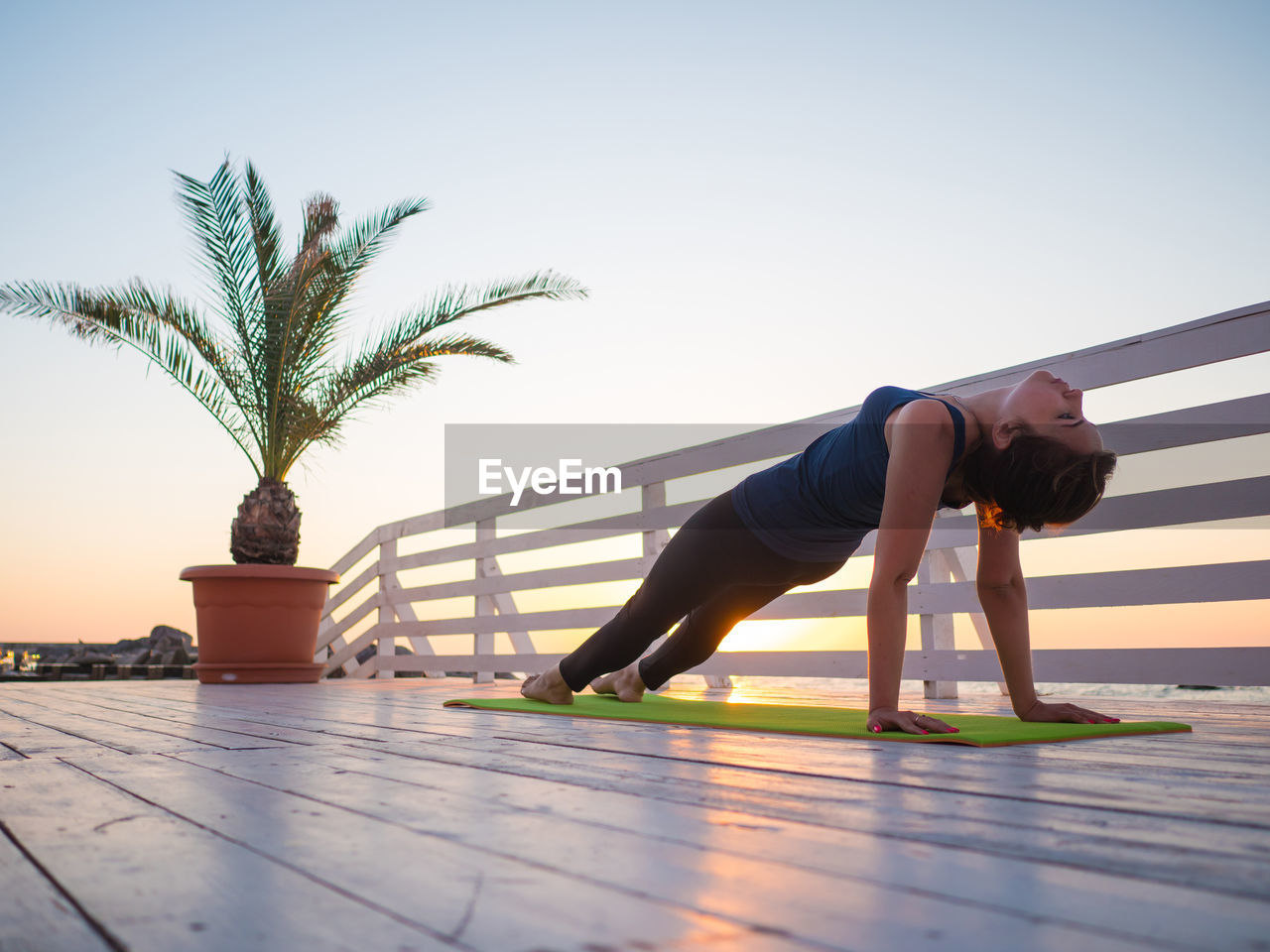 Full length of woman doing yoga on promenade against clear sky during sunrise