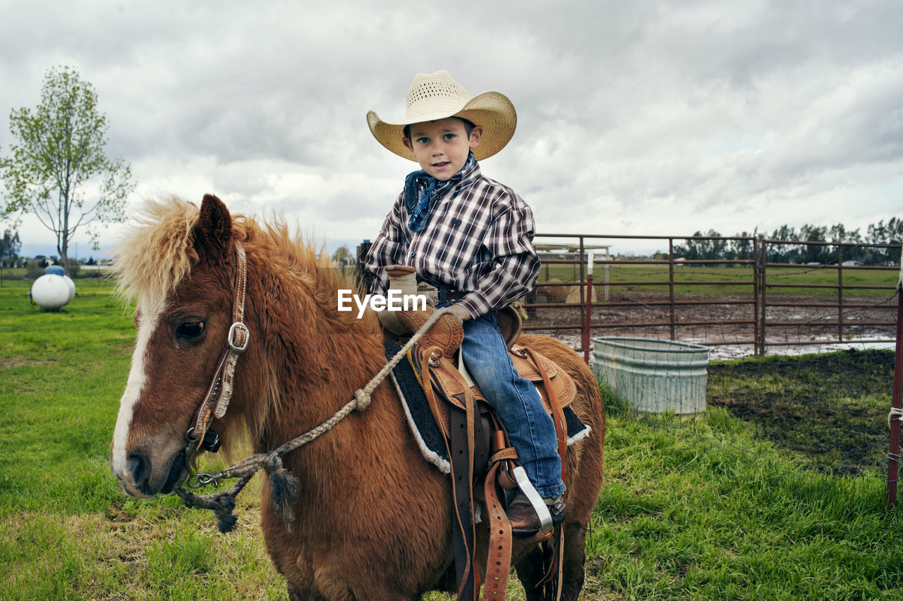 Portrait of cute cowboy riding horse on ranch