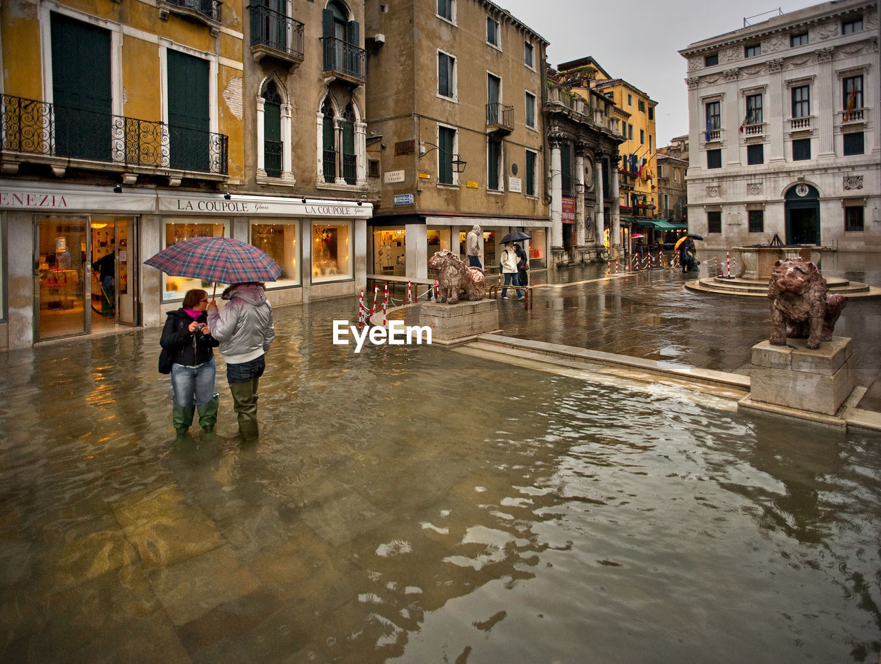 People with umbrellas on water filled walkway during flood at piazza san marco