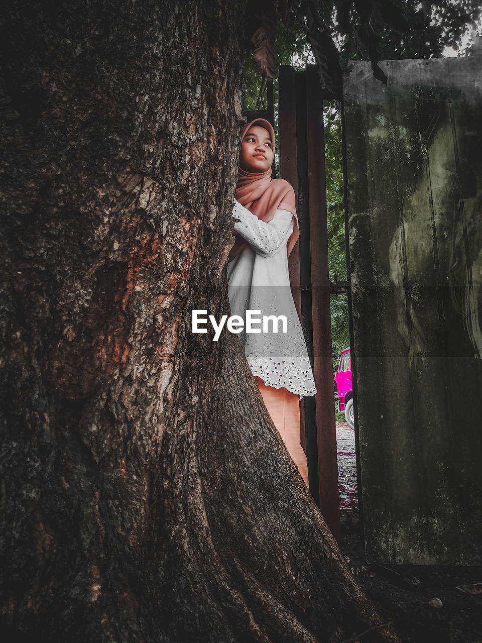 PORTRAIT OF BEAUTIFUL WOMAN STANDING BY TREE TRUNK