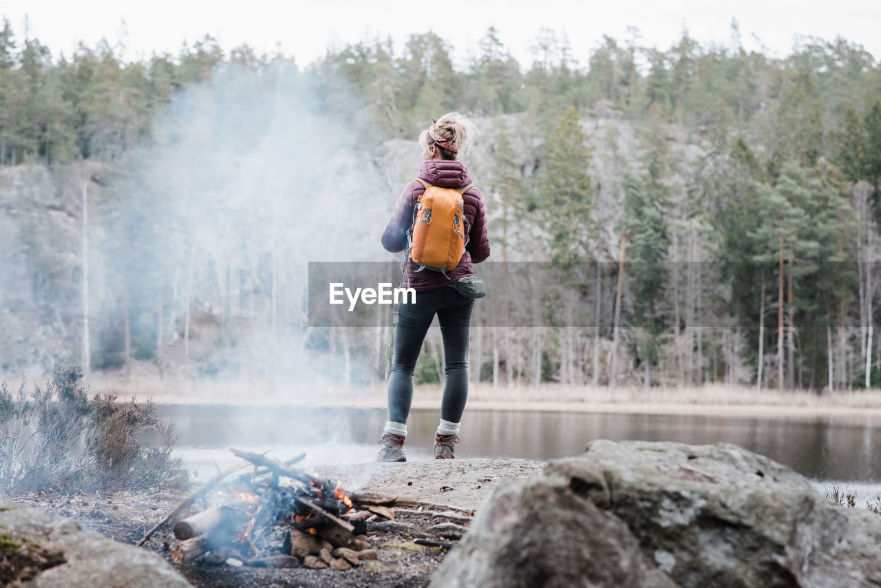 Woman standing on a rock by a campfire whilst hiking in sweden