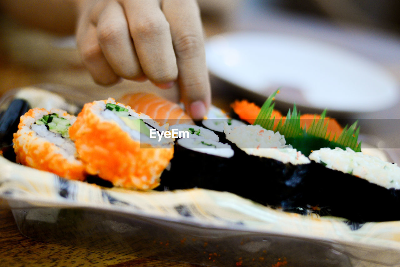 Cropped hand taking sushi served in plate