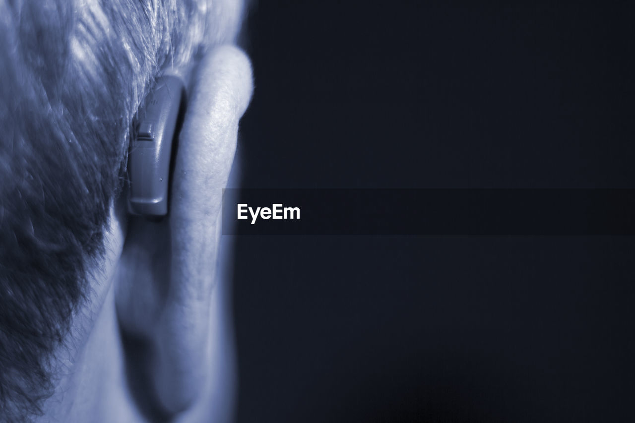 Rear view of man with hearing aid against black background