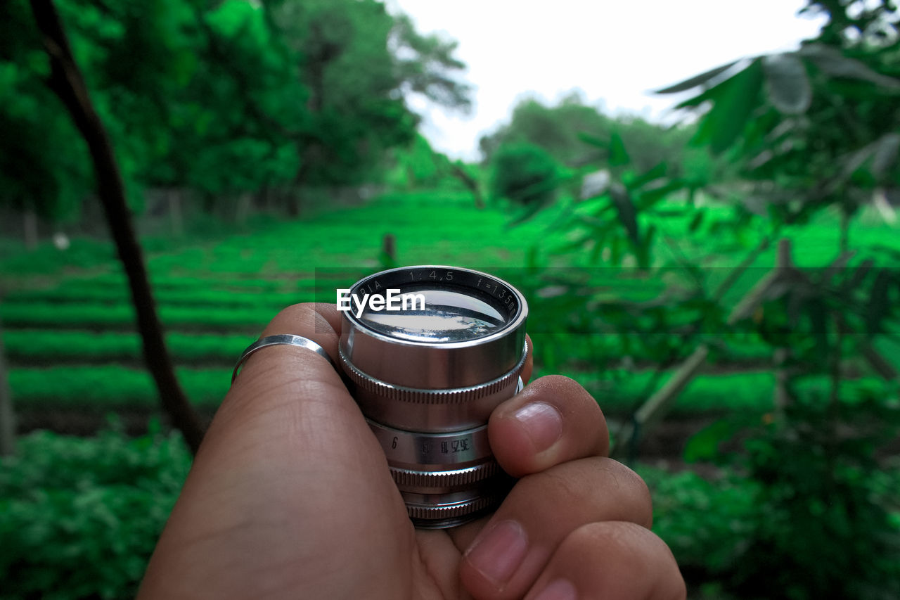 Close-up of cropped hand holding lens by farm