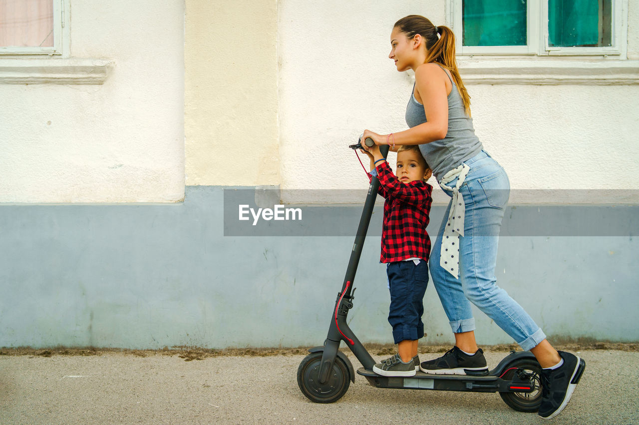 Woman and boy riding electric push scooter on street