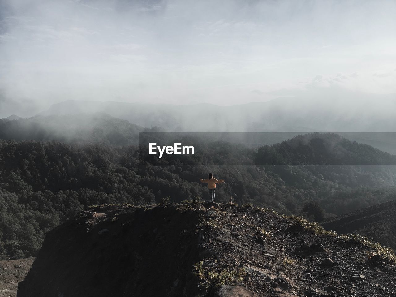 Rear view of woman standing on mountain against sky in foggy weather