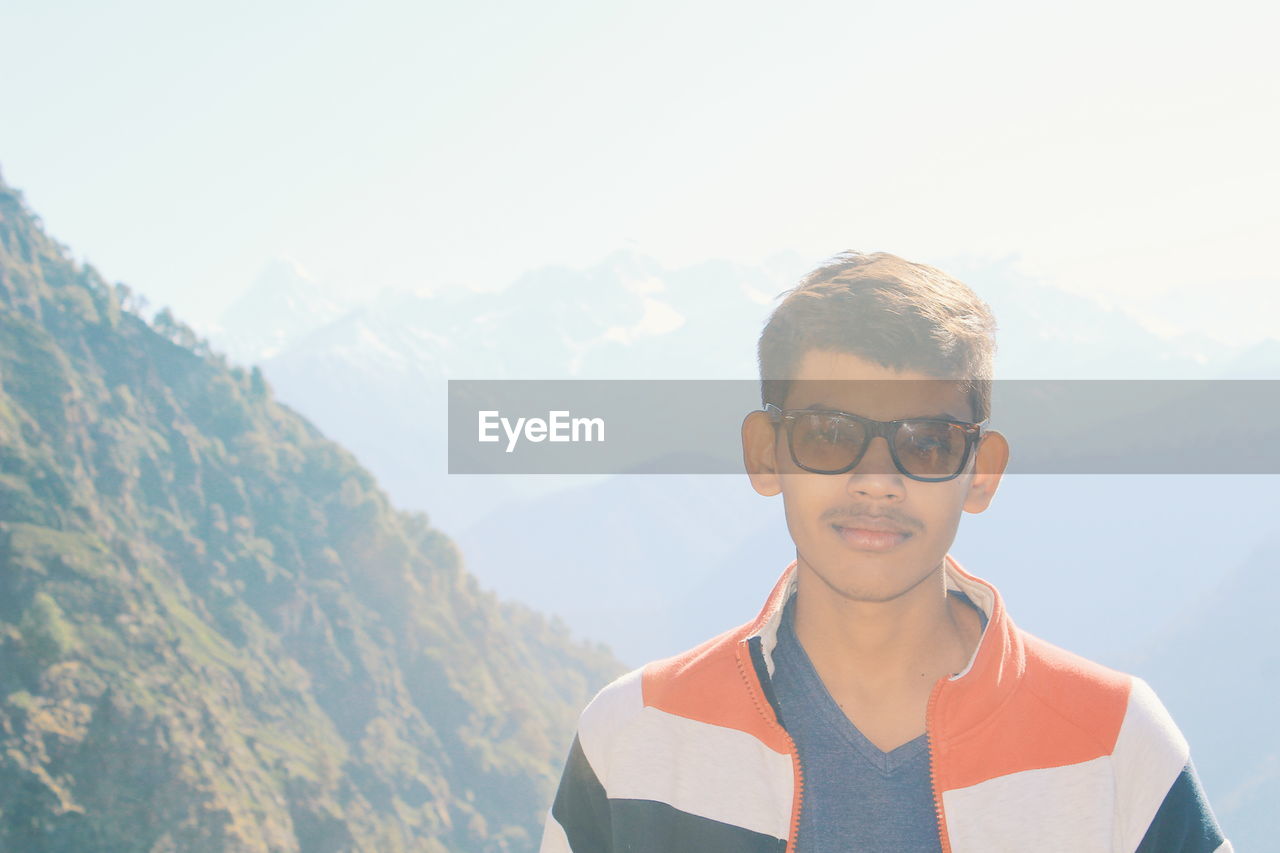 Portrait of boy standing in front of mountain against sky