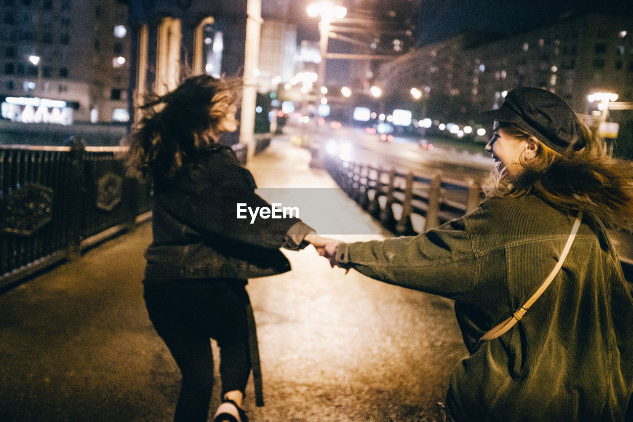 Smiling friends walking on road in city at night