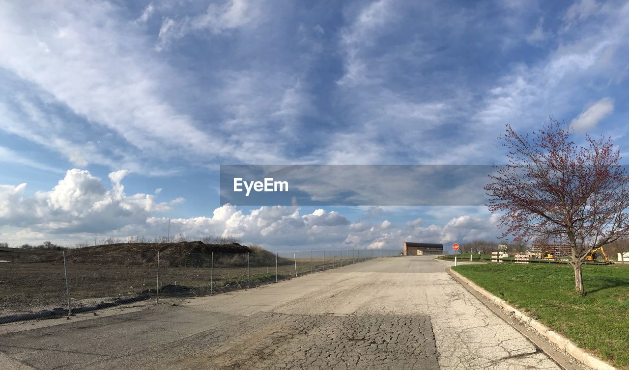 Empty road amidst field against sky