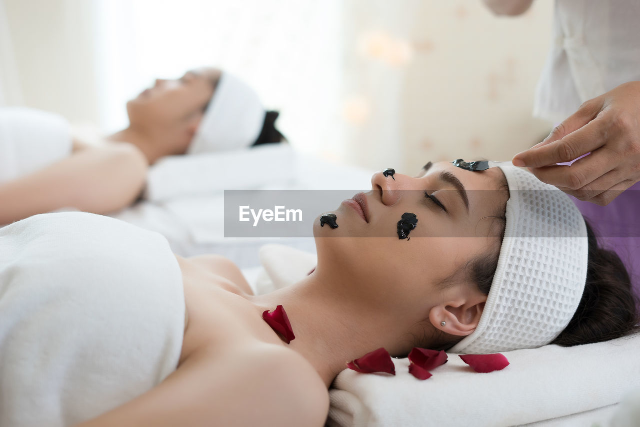 Cropped hand of massage therapist applying facial mask on young woman face in spa