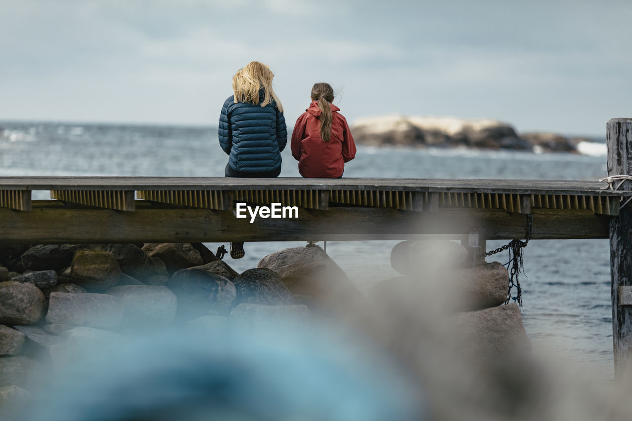 Mother and daughter sitting on jetty