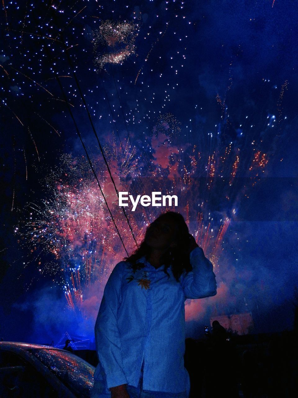 Woman standing by car against fireworks in sky at night