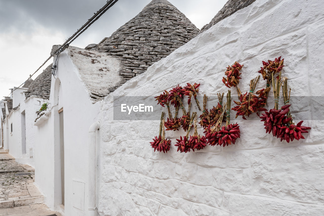 Red chili peppers drying on wall of trulli house against cloudy sky