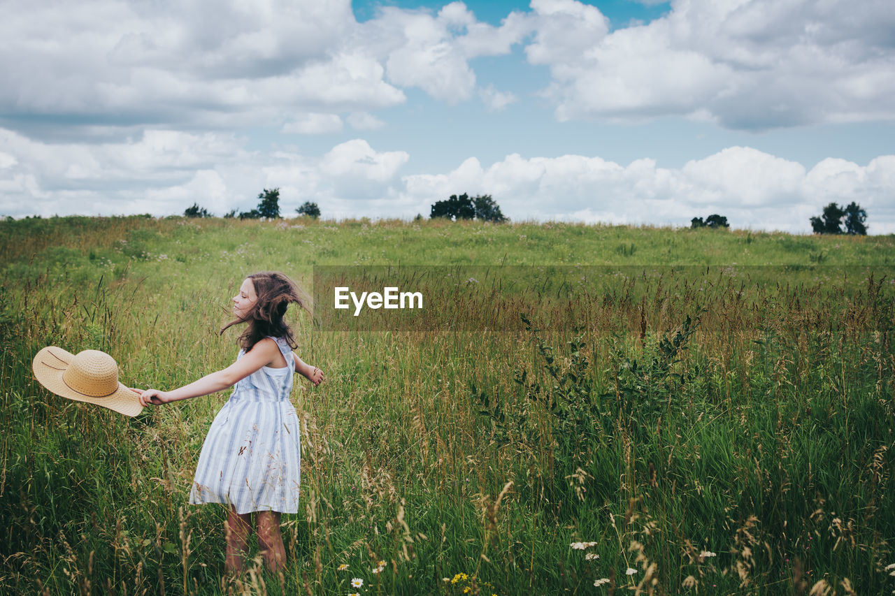 Teen girl twirling in a grassy field on a cloudy summer day